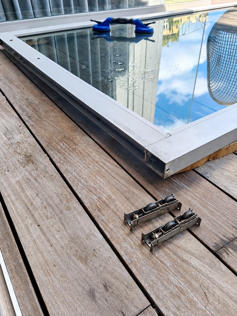 Sliding door panel lifted out and laid flat, with its two rollers removed beside it.