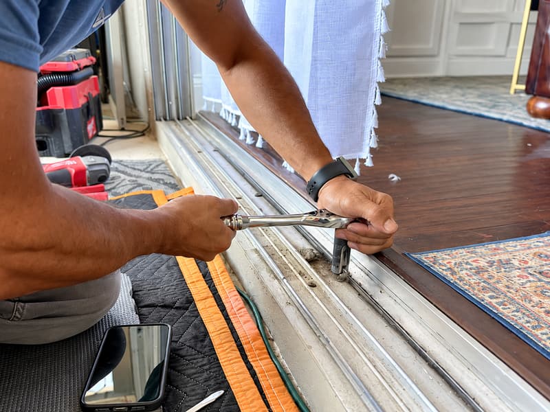 Technician working on the bottom track of a sliding glass door with pliers.