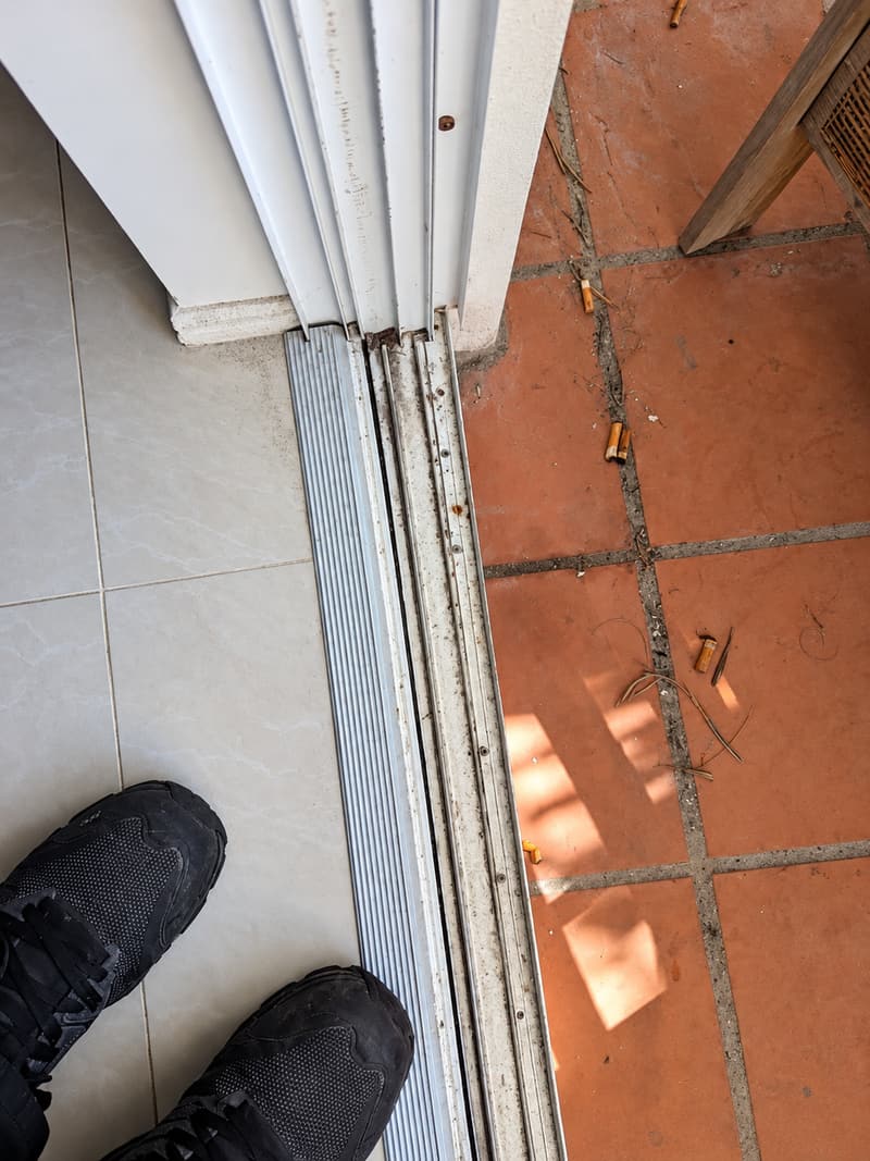 Worn sliding door track with dirt and debris along the threshold.